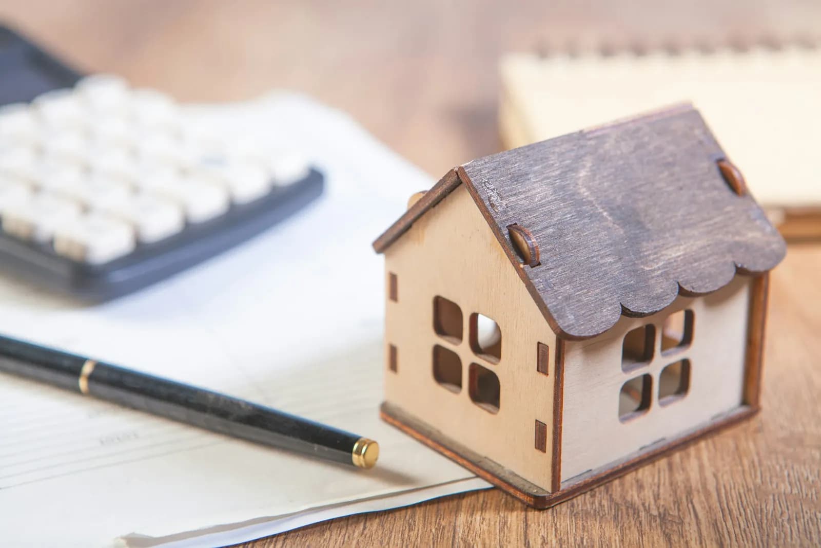 Maqueta de una casa de madera junto a una calculadora y un bolígrafo